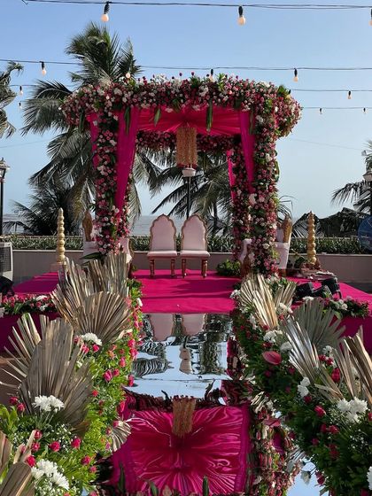 A vibrant beachside mandap in shades of pink. The mirror aisle and bohemian dried palm accents create a beautiful contrast against the ocean backdrop.