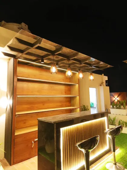 A sleek and modern bar setup under a pergola, with a dark marble countertop and well-lit wooden shelves for displaying glassware and bottles.