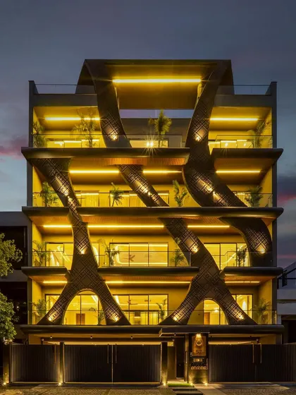 The wave-form facade at night, where lighting accentuates the fluid, sculptural elements. The design creates a dramatic and elegant statement, highlighting the unique concrete grooving and stone finish.