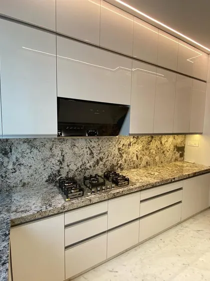 Another view of the pristine acrylic kitchen at Lodha World Tower. The handle-less design and continuous lines of the cabinetry create a sophisticated and uncluttered environment, enhanced by integrated profile lighting.