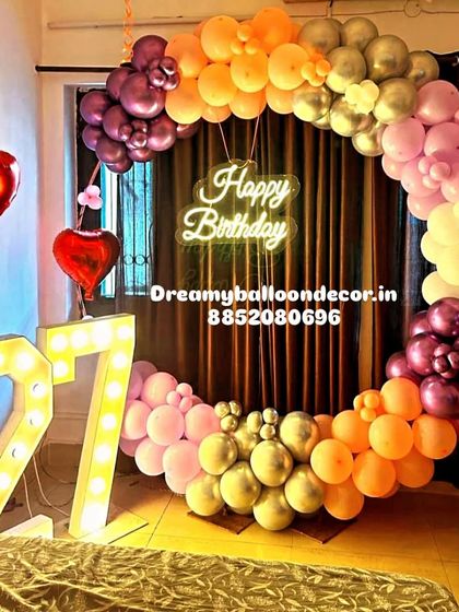 A colorful and trendy birthday setup for a 27th birthday. The balloon ring uses a beautiful gradient of sunset colors, paired with large light-up marquee numbers.