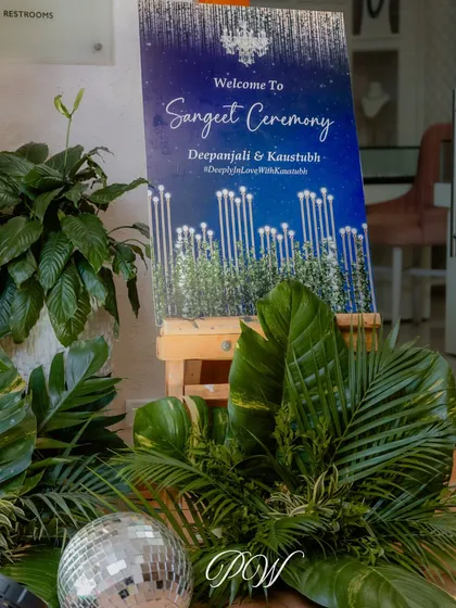 A sleek and modern welcome sign for a Sangeet ceremony, using a starry night theme and surrounded by lush greenery and a single disco ball for a hint of glam.