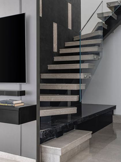 The staircase in this duplex is more than functional; it's a stylish centerpiece. The combination of concrete-finish steps, a glass railing, and a dark marble base creates a piece of art that connects the two levels.