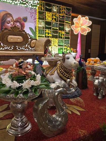 A close-up of the offering table for a Krishna-themed ceremony, with a central cow prop and a Ganesha idol.