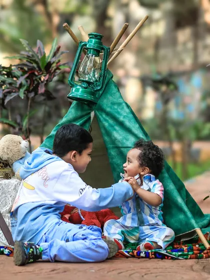 Two brothers share a sweet moment inside a small green play tent set up outdoors. The older brother gently interacts with his younger sibling, a perfect example of the unscripted sibling bonds I aim to capture.