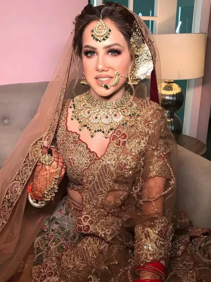 A smiling bride, looking radiant in her wedding attire. The jewellery set includes a statement choker, matha patti, and a delicate nath.