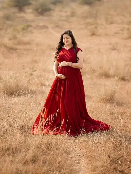 A stunning solo portrait featuring one of my flowing maternity gowns. The vibrant red stands out beautifully against the rustic, sunlit field, creating a dramatic and elegant look.