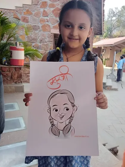 A cute girl with her finished portrait, complete with her name "Khushi" in beautiful calligraphy. It's a perfect memento from a fun day.