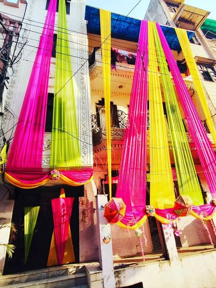 A low-angle shot of a house decorated with bright pink, yellow, and lime green drapes, creating a canopy of colour.