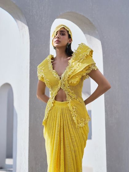 Tradition, retold through structure. This yellow ensemble features a sculpted jacket with dramatic shoulders and a matching draped skirt, giving heritage a shape that feels distinctly now.