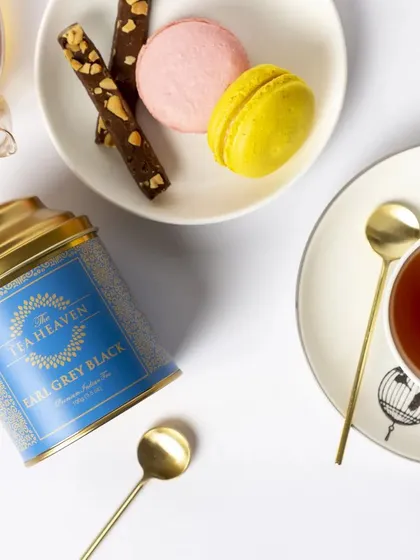 This top-down flat lay of Earl Grey tea is styled for a modern, elegant brand. The clean white space, paired with colourful macarons and gold spoons, creates a sophisticated image ideal for social media or a brand lookbook.