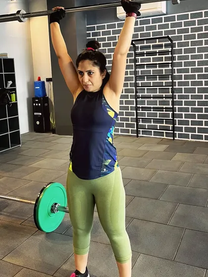 This is why weight training is crucial. I'm demonstrating an overhead press with a barbell, a compound movement that strengthens the shoulders, arms, and core all at once.