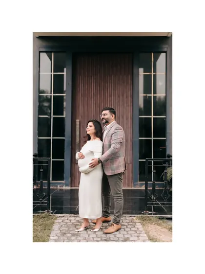 An expecting couple posing outdoors in front of a modern building with large glass-paned doors. This shot blends natural light with contemporary architecture for a stylish maternity portrait.