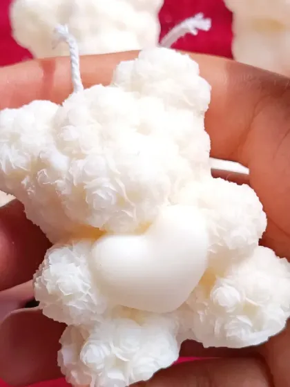 A close-up of a single small teddy bear candle, showing its textured, fluffy appearance.