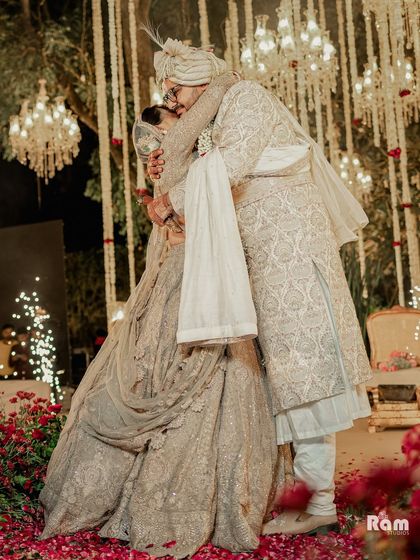 A grand and romantic moment as the groom hugs his bride on stage, surrounded by a carpet of rose petals and under a canopy of chandeliers.