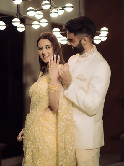 A playful moment showing off the new engagement ring. The excitement and joy are palpable in this candid shot, beautifully lit by a modern chandelier, adding a touch of glamour to the celebration.