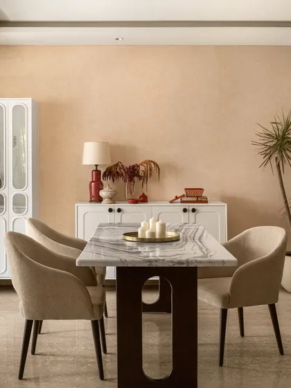 I believe a dining room should be the heart of the home, a place that naturally draws people together. Here, the warm, earthy tones on the walls and the elegant marble tabletop create an inviting atmosphere for shared meals and conversations. The space is completed with a simple white crockery unit and touches of red and brass, making it feel cherished and lived-in.