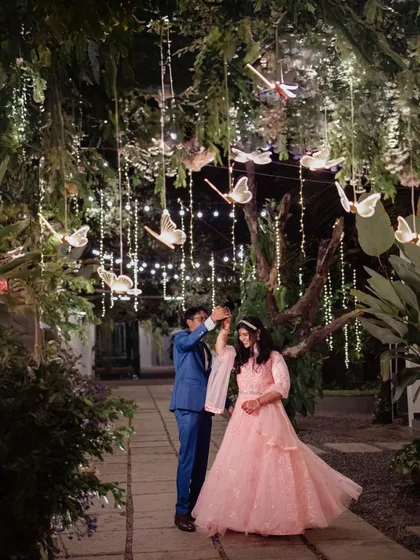 A fairytale-like engagement shoot at night. The couple dances under trees adorned with fairy lights and butterfly decorations, creating a truly magical and romantic scene.