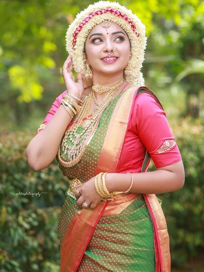 A joyful outdoor portrait of a bride wearing the Sharadha Jalli. The natural light and green background make the traditional attire pop.
