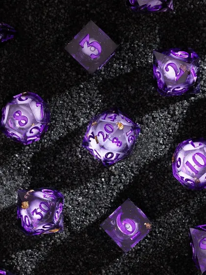 A textured shot of purple dice on a bed of black sand. The contrast between the sparkling purple dice and the dark, gritty sand creates a visually striking and moody image.