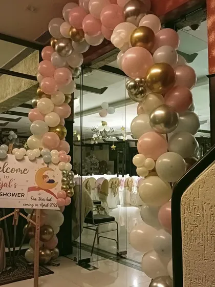 A beautiful balloon arch makes for a grand entrance. This organic arch, in shades of pink, white, and chrome gold, welcomed guests to a baby shower and featured a personalized sign with the mother's name and due date.