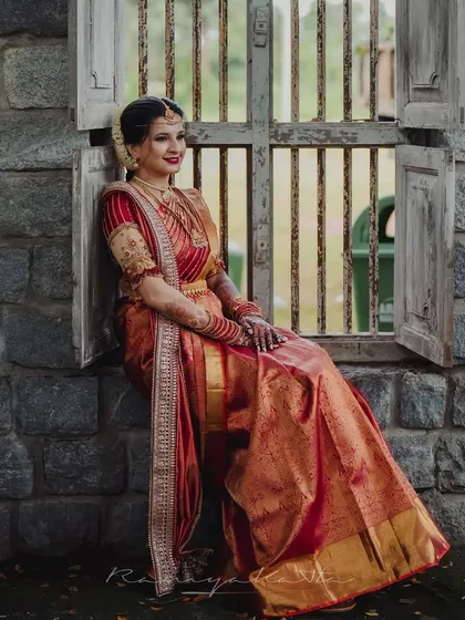 A moment of quiet elegance. This bride is the picture of grace in a traditional red and gold Kanjeevaram silk saree, paired with a bespoke embroidered blouse. The rich texture of the silk and the detailed craftsmanship of the blouse create a timeless bridal look.