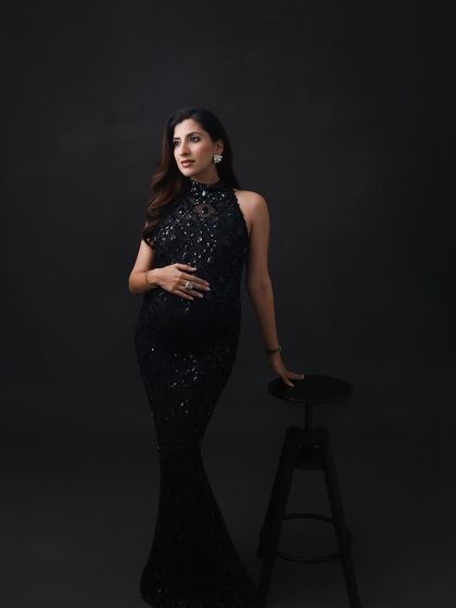 A thoughtful and elegant pose. The dark, minimalist setting allows the sparkling gown and the mom-to-be's quiet confidence to take center stage.