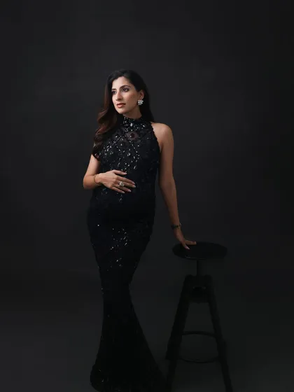 A thoughtful and elegant pose. The dark, minimalist setting allows the sparkling gown and the mom-to-be's quiet confidence to take center stage.