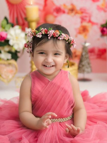 A close-up of a smiling princess. Her floral crown and the soft pink background create a beautiful and delicate portrait.