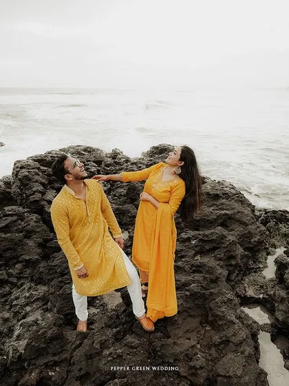 A playful and candid moment on the rocks by the sea, capturing the fun-loving nature of their relationship.