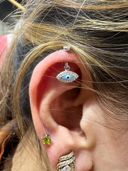 An evil eye hanging to bring protection and style, paired with a vibrant green stud for a pop of color.