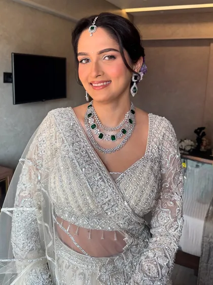 A happy, glowing bride. The makeup is kept minimal and radiant to complement her intricate ivory outfit and stunning emerald jewelry.