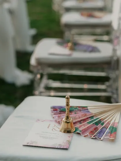 Small details make a big impact. A small brass bell and a colorful fan are placed on each guest's seat, providing a charming and practical favor for the outdoor ceremony.