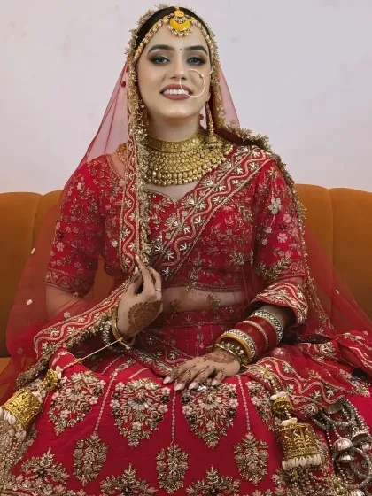 A full-length shot of the bride seated comfortably, showcasing her beautiful red lehenga and traditional gold jewelry.