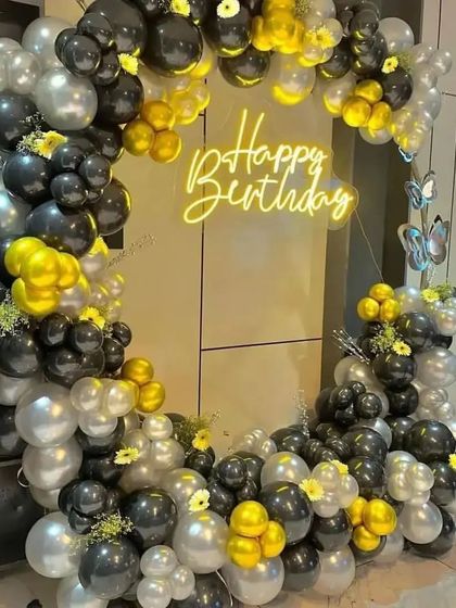 A sophisticated birthday balloon ring in a black, yellow, and silver color scheme, accented with small flowers and a neon sign.