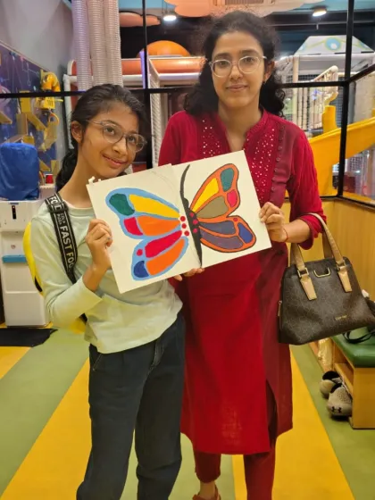 A mother and daughter proudly display the colorful butterfly painting they created together during one of our guided art sessions.