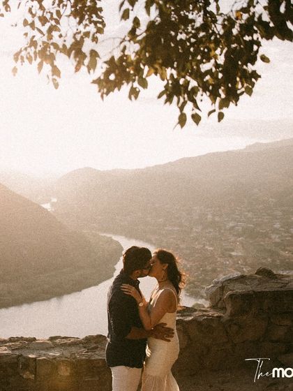 A romantic kiss overlooking a winding river and valley in Georgia. The hazy, sun-drenched landscape creates a soft, dreamy backdrop for this intimate moment.