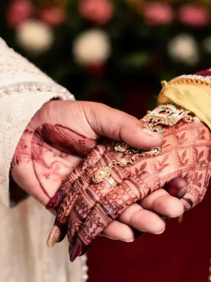 A close-up of the couple's hands joined during the wedding ceremony. This image, focusing on the bride's intricate mehndi and the way their hands are held, symbolizes their union and the promises being made.