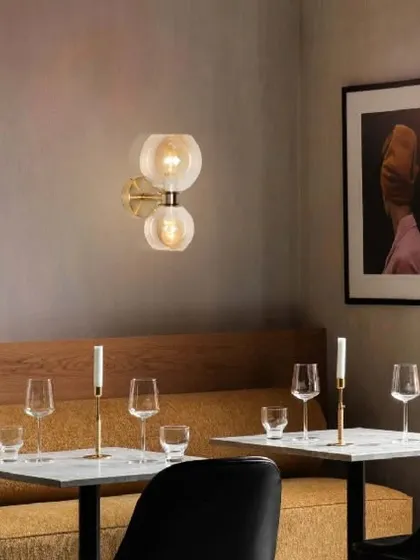 This antithetical wall lamp combines antique brass with two glass globes for a modern, elegant look. It's perfect for adding a touch of sophisticated lighting to a dining area, hallway, or bedroom.