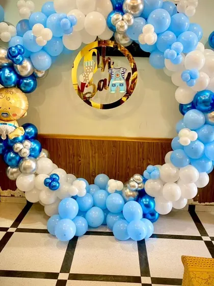 An "Oh Baby!" themed decoration for a baby boy's shower. The circular backdrop is made of blue, white, and chrome silver balloons, with a cute baby boy foil balloon and a custom gold sign.