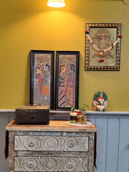 A cozy corner featuring traditional Indian art and a rustic carved chest of drawers. This space shows how we love to mix different styles and textures to create a home that feels collected and personal.