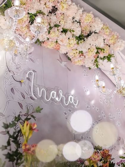 A detail shot of the neon sign with baby Inara's name, set against the floral backdrop and sparkling chandeliers. This modern touch added a personalized and celebratory element to the decor.