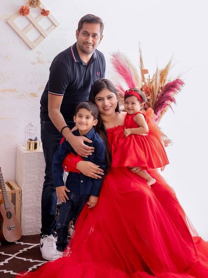 This portrait showcases a family of four in a bright, airy studio setting. The mother's flowing red dress adds a pop of color, while the relaxed pose captures a moment of family unity.