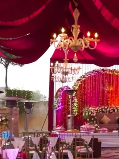 A grand wedding mandap with a backdrop of red crystal strings and a massive floral arch. The draped ceiling and chandeliers add to the magnificent and royal feel of the setup.