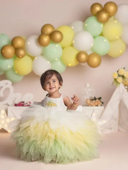 "I just turned one!" This little girl looks like a princess in her fluffy yellow and green dress, surrounded by a beautiful pastel balloon arch.