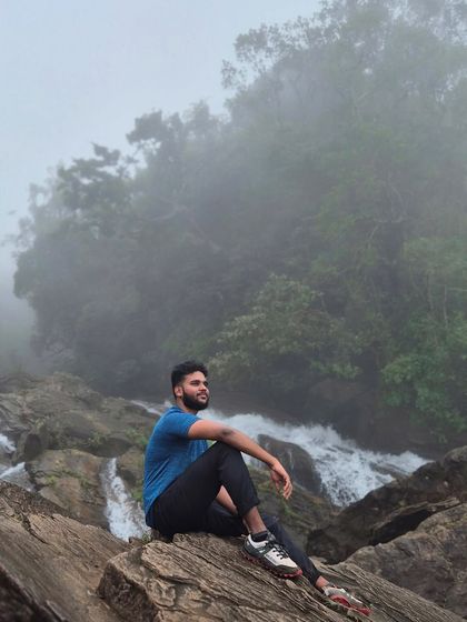 A trekker sits on a rock by a stream, surrounded by the misty forest of Bandaje.
