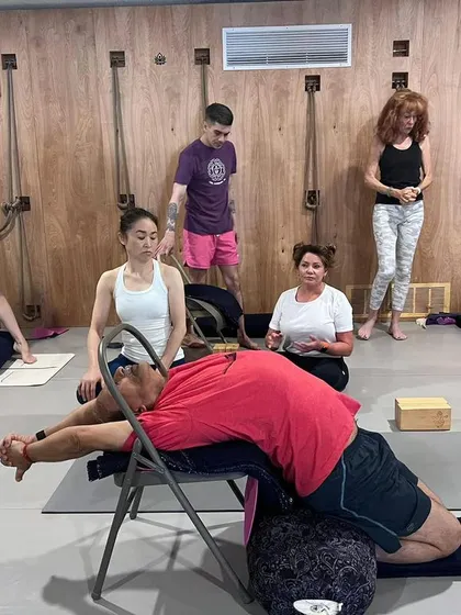 Leading a class at Yoga Kurunta in San Antonio, Texas, with a demonstration of a restorative pose using a chair and bolster.