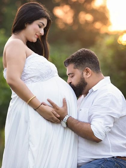 A classic and loving pose where the father-to-be kisses the baby bump. This outdoor shot, taken in soft natural light, is full of warmth and anticipation.