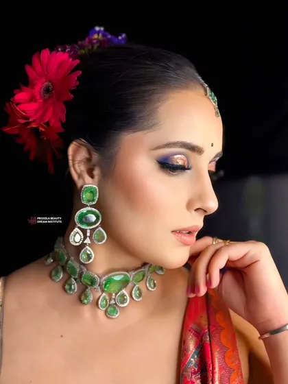 Grace in every glance. This elegant look features a pop of blue under the eye, beautifully complementing the emerald green jewelry and red outfit.