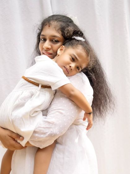 A tender hug between a mother and her daughter against a simple white backdrop set up outdoors.